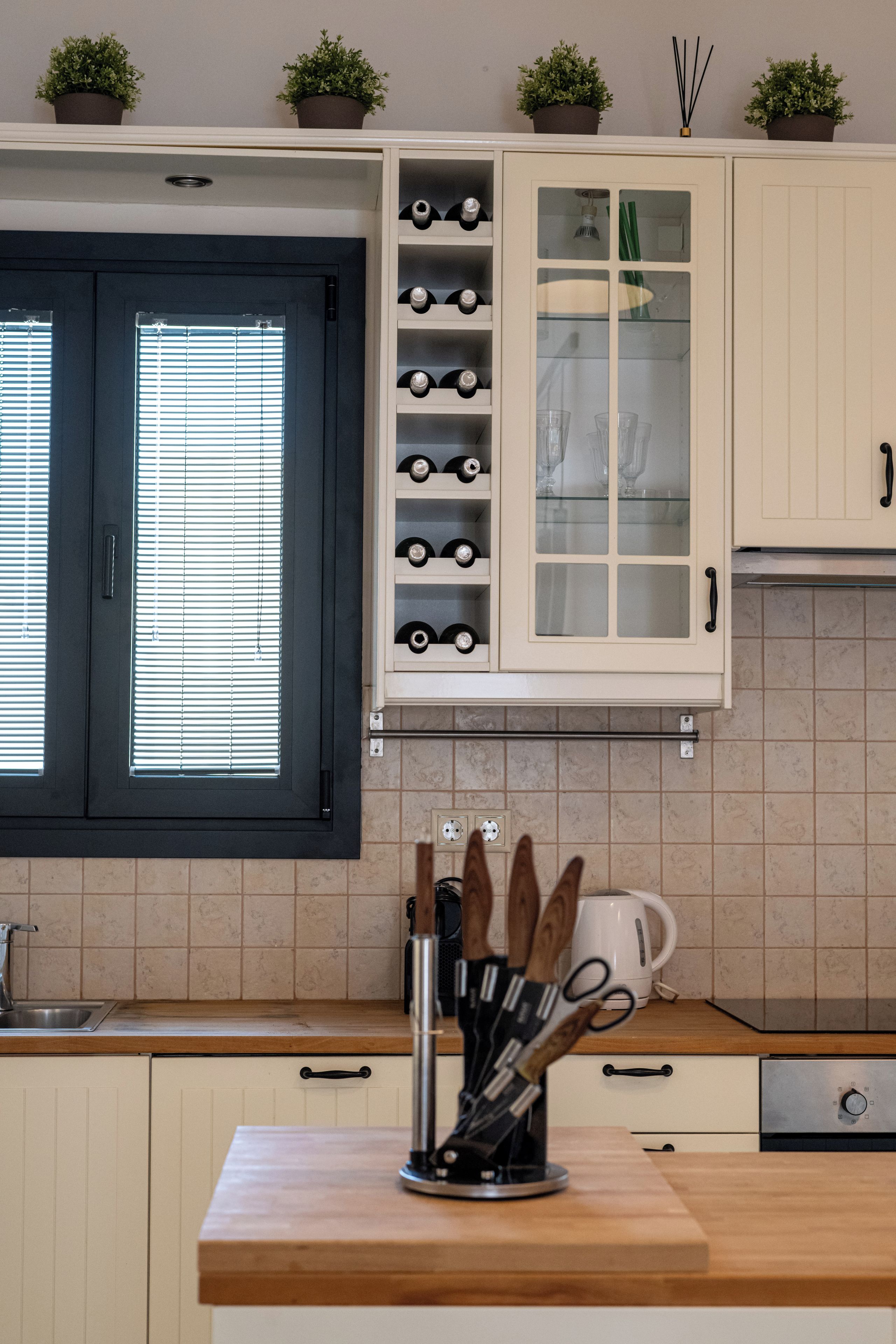 A kitchen with white cabinets, a wine rack, and a window with blinds.