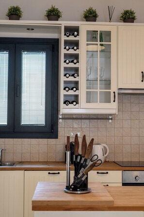 Une cuisine avec des meubles blancs, un meuble à bouteilles et une fenêtre avec des stores.