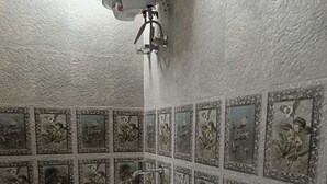 Ein Badezimmer mit einem weißen Waschbecken, einer Toilette und einer Dusche. Die Wände sind mit floralen Mustern gefliest.