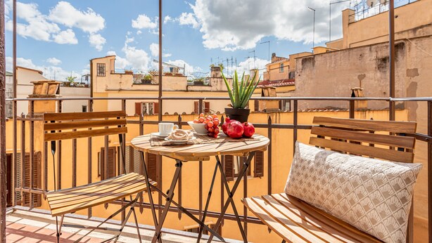 Een balkon met een houten tafel, stoelen en een plant in pot.