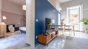 Een moderne hotelkamer met een groot bed, een houten console, een televisie, een zithoek met stoelen en een groot raam met uitzicht over de stad.