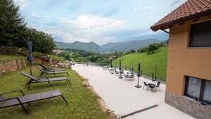 Une terrasse dotée de chaises longues et de tables, offrant une vue sur une vallée avec des montagnes en arrière-plan.