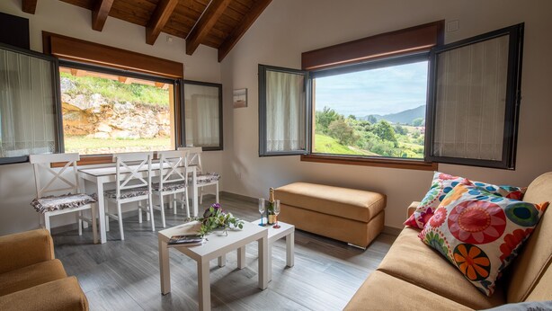 Un salon moderne avec un coin repas, de grandes fenêtres avec des rideaux et une vue sur la campagne.