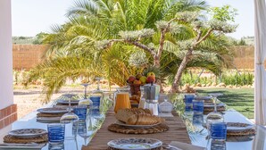A table set for breakfast with plates, glasses, and a fruit basket. - Villa Colona, Los Algarbes J22g+94 (Los Algarbes- La Carlota)