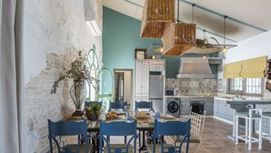 A dining area with a table set for four, surrounded by blue chairs. A large vase with plants is on the table. - Villa Colona, Los Algarbes J22g+94 (Los Algarbes- La Carlota)