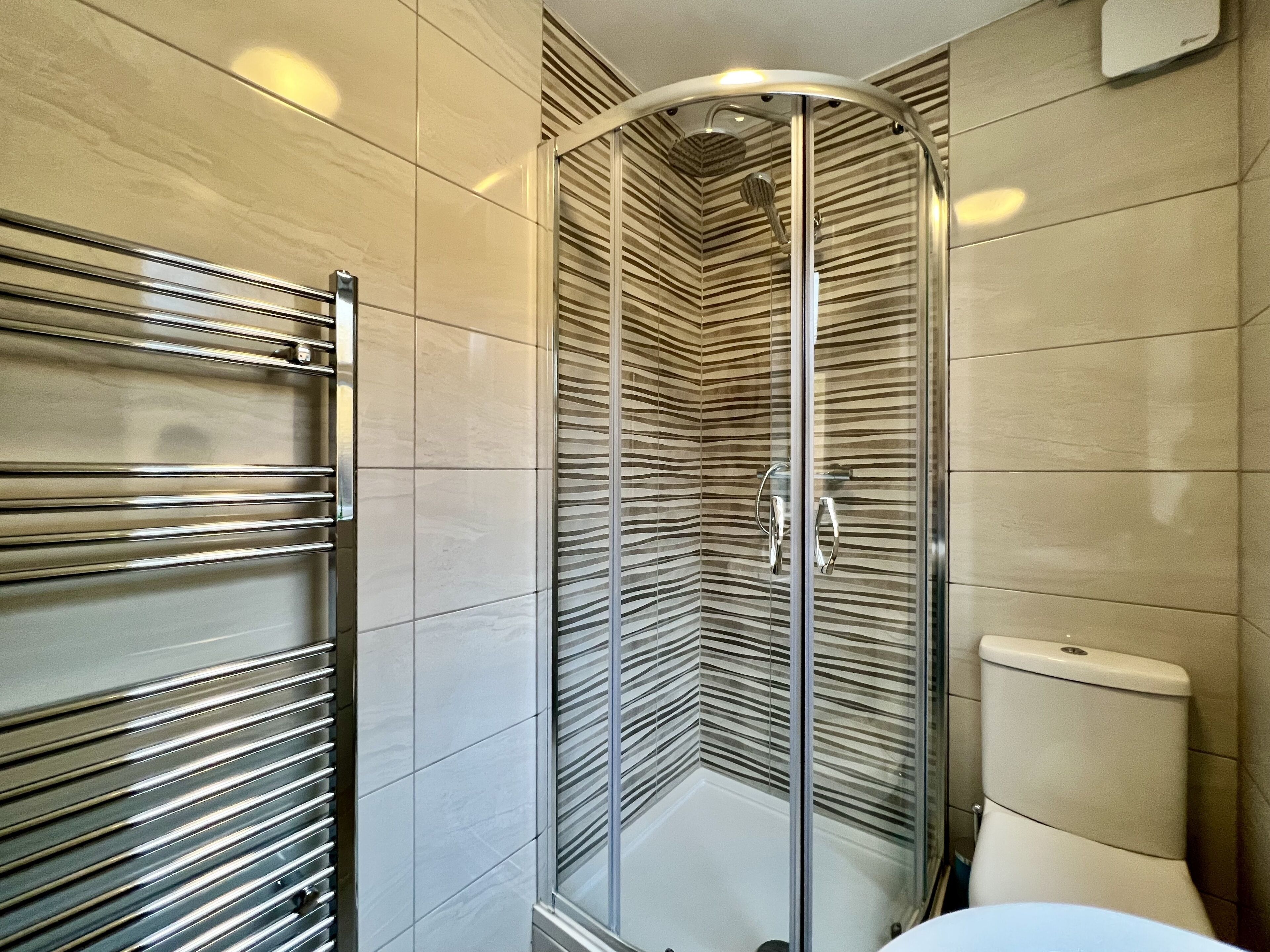 A modern bathroom with a glass shower enclosure, a chrome towel rack, and a toilet.