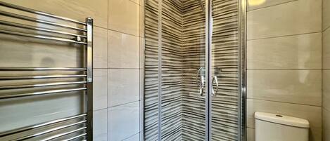 A modern bathroom with a glass shower enclosure, a chrome towel rack, and a toilet.