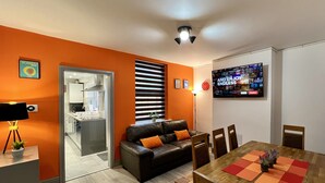 Un saló modern amb un sofà de pell negra, taula de dinar de fusta i cuina visible a través d'una porta oberta.