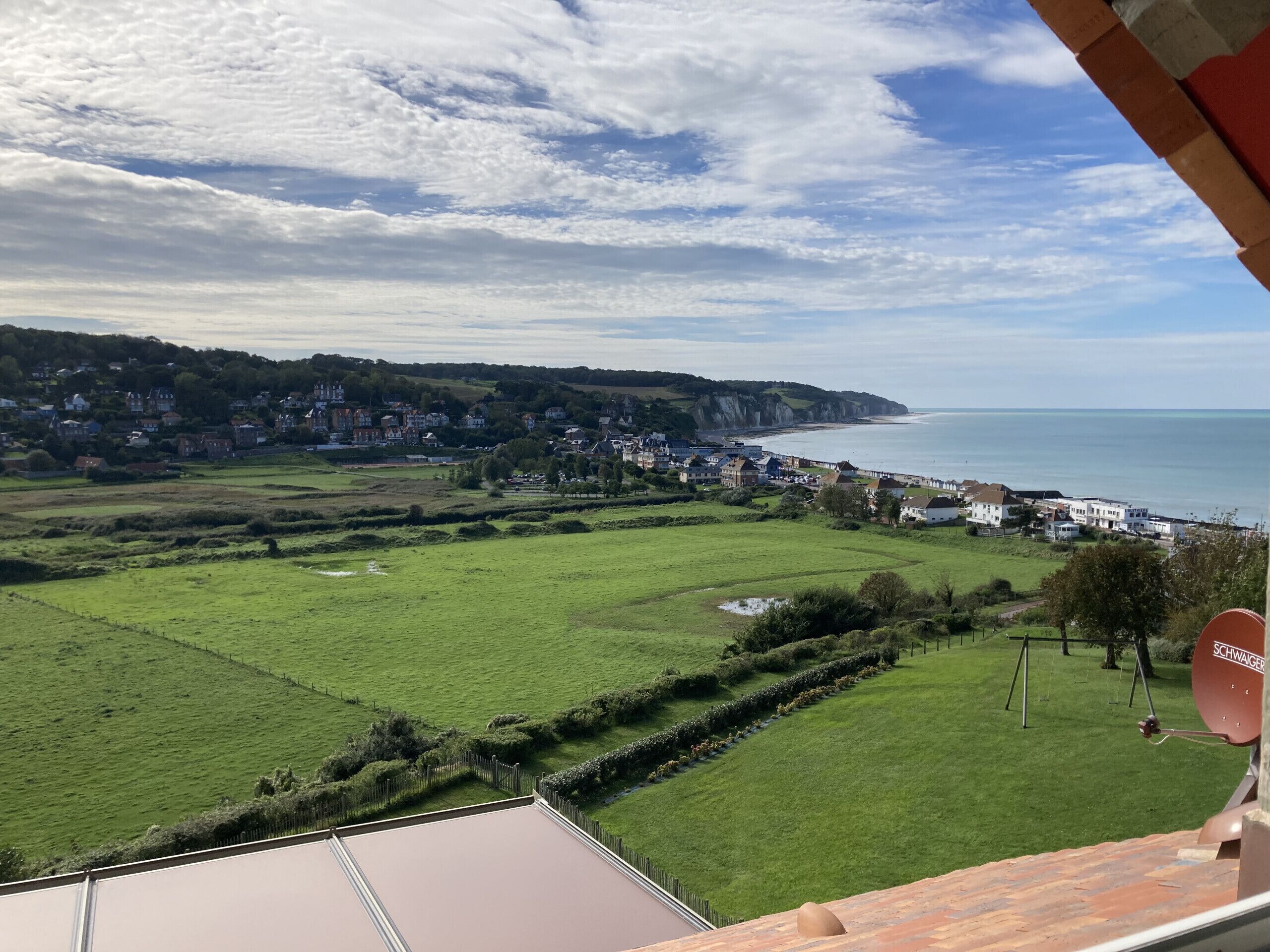 A coastal town with a view of the sea, green fields, and a mix of residential and commercial buildings.