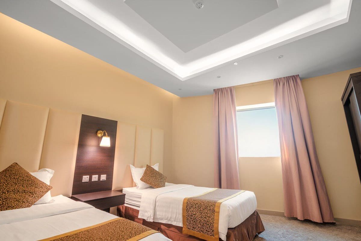 A hotel room with two beds, a skylight, a large window with curtains, and a wall-mounted light fixture.
