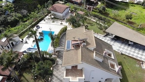 Una casa de dos pisos con piscina, terraza techada y jardín.
