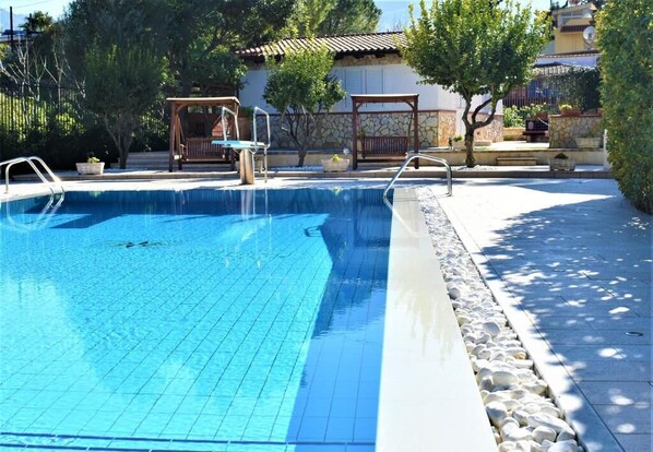 A swimming pool with a tiled deck, a wooden deck area, and a stone wall in the background.
