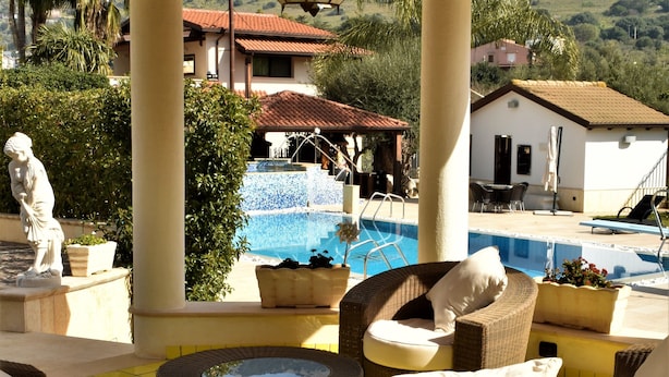 Un espacio de estar techado al aire libre con mobiliario de mimbre, una piscina y una estatua.