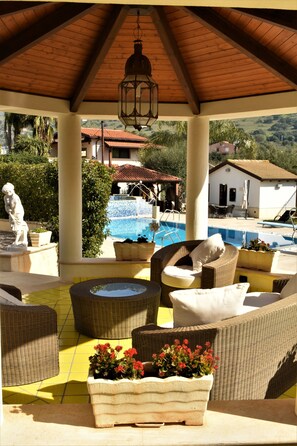 A covered outdoor seating area with wicker furniture, a pool, and a statue.