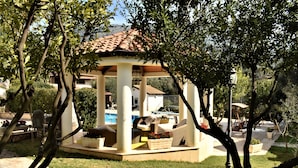 Un mirador con techo de tejas, rodeado de vegetación y una zona de piscina.