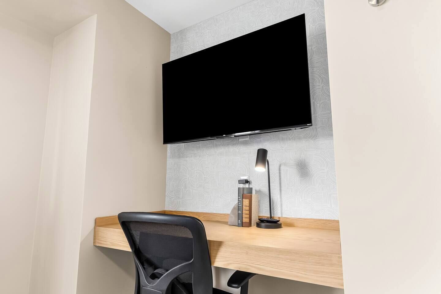 Despatx modern amb un televisor de pantalla plana penjat a la paret, un escriptori de fusta, una cadira de oficina negra, una làmpada d'escriptori i una ampolla d'aigua.