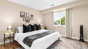 Ein Schlafzimmer mit einem großen Bett, Nachttischlampen, einem Fenster mit Vorhängen und einem Standheizgerät.