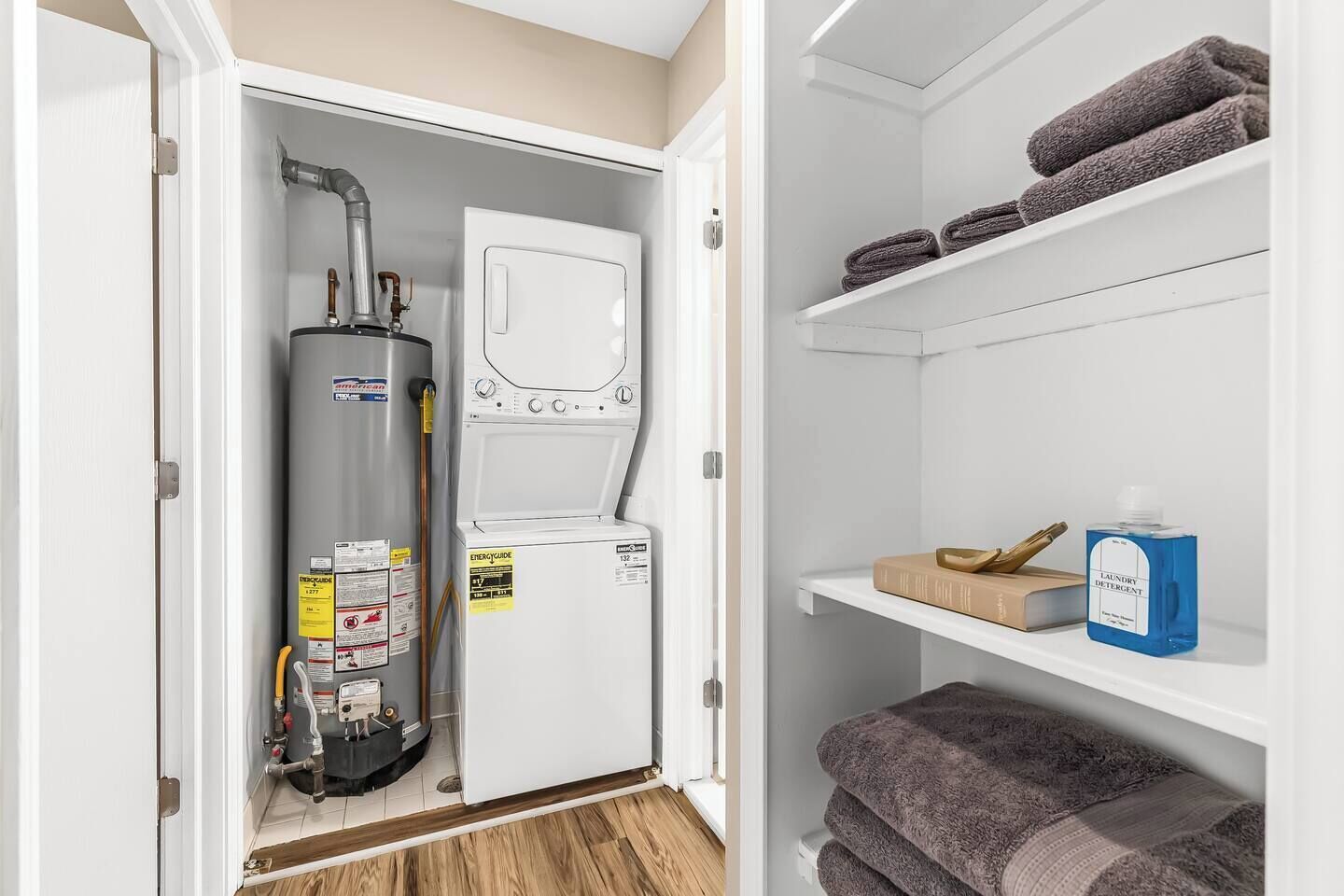 A laundry room with a water heater, a washing machine, and shelves with towels and laundry detergent.