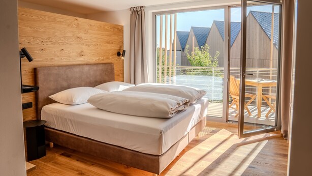 A bedroom with a large bed, wooden headboard, and a view of a balcony with outdoor furniture.