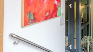 A hallway with a red abstract painting, a handrail, and a door leading to a room with a dark interior.