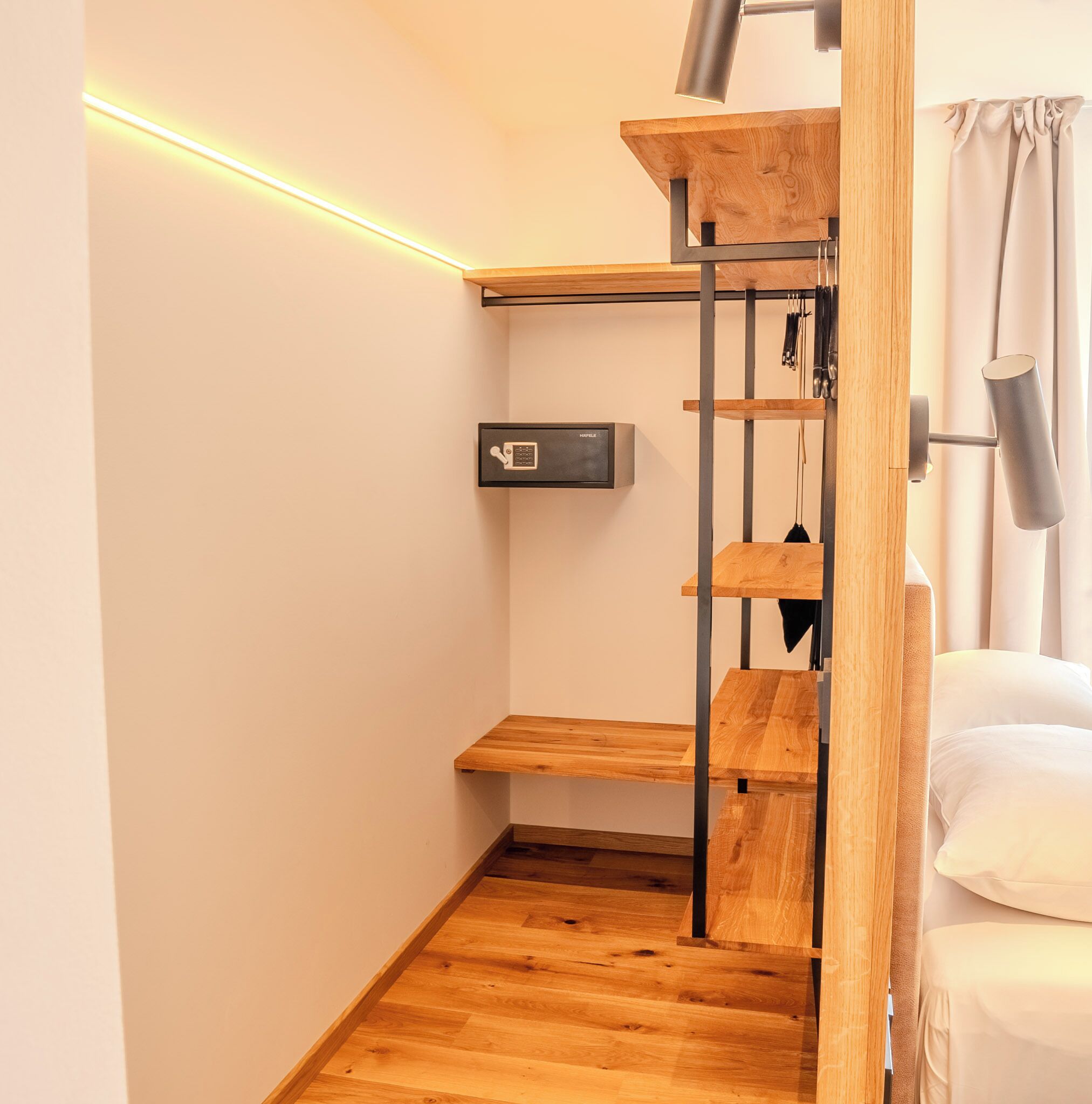 Una habitación compacta con piso de madera, un estante empotrado, una caja fuerte en la pared y una cama con cortinas.