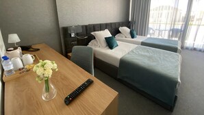 Quarto de hotel com duas camas, uma escrivaninha de madeira com um vaso de flores, um controle remoto e uma luminária.
