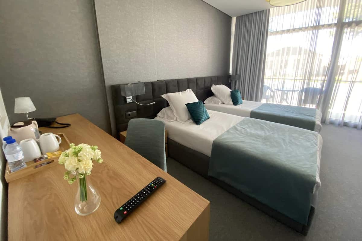 Ein Hotelzimmer mit zwei Betten, einem Holztisch mit Blumenvase, einer Fernbedienung und einer Lampe.