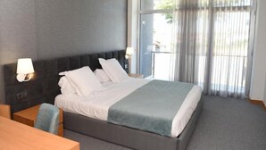 Quarto de hotel moderno com uma cama grande, uma escrivaninha e vista para uma varanda.