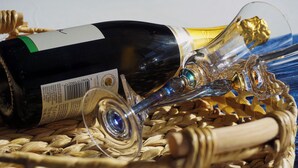 Uma garrafa de vinho e um copo sobre uma superfície trançada.