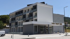 Um hotel moderno com telhado plano, várias varandas e uma placa com o texto 