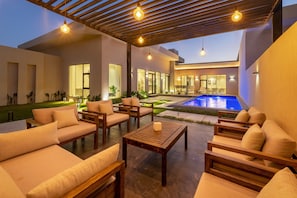 Ein moderner Außenbereich mit Sofas, Tischen, einem Pool und einem Gebäude mit großen Fenstern.