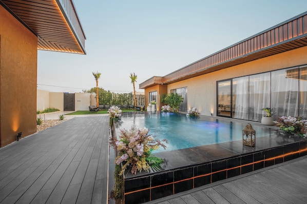 Un área de piscina moderna al aire libre con cubierta de madera, rodeada por un muro bajo con planta trepadora.