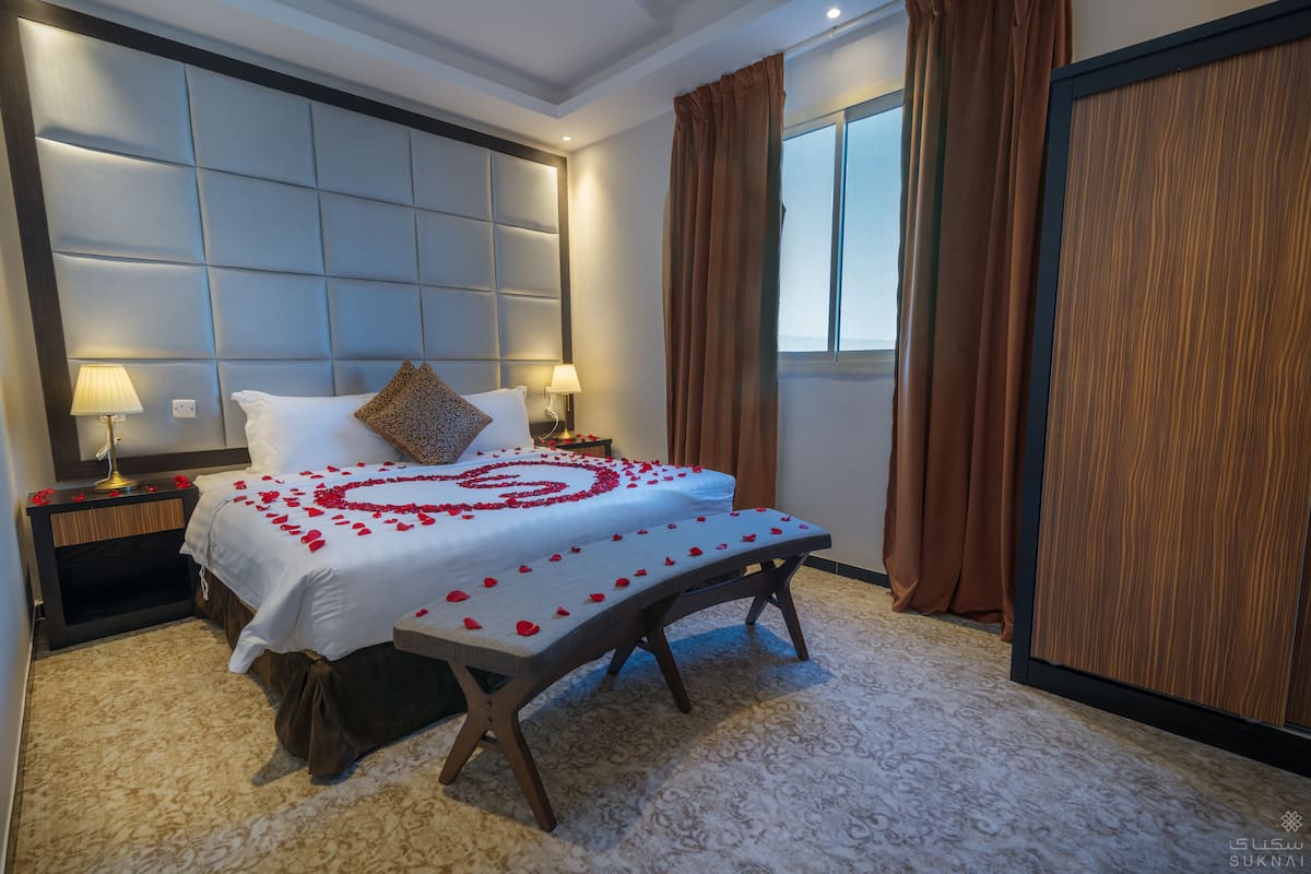 Una habitación de hotel con una cama grande, un banco, una mesita de noche y un armario.