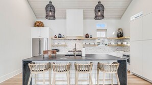 Una cocina moderna con una isla central, taburetes de bar, lámparas colgantes y electrodomésticos integrados.