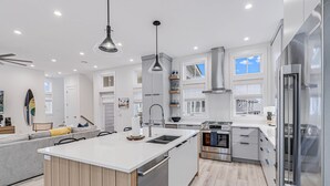 A modern kitchen with a central island, stainless steel appliances, and a grey sofa in the living area.
