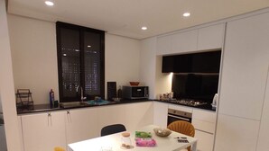 A modern kitchen with white cabinets, a dining table with chairs, and a window overlooking a cityscape. - Ayla Vacation home 
 (Aqaba)