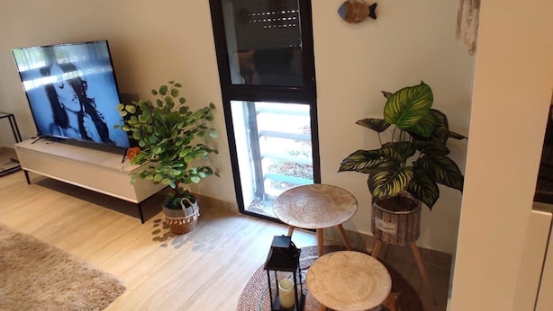 A modern living room with a TV, potted plants, decorative fish, and a round wooden table with a candle. - Ayla Vacation home 
 (Aqaba)
