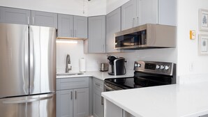 A modern kitchen with grey cabinets, stainless steel appliances, and a white countertop. - Oceanfront: Beach, Sand and Views at Coral Reef! (North Topsail Beach)