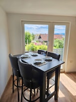 Un comedor con una mesa dispuesta para cuatro, sillas y vistas a un barrio residencial a través de un ventanal.