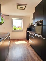A modern kitchen with a built-in oven, a window with a view of greenery, and wooden flooring.