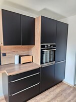 A modern kitchen with black cabinets, a wooden countertop, and a built-in oven.