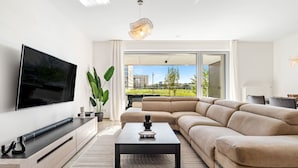 Una sala moderna con un televisor de pantalla plana, un sofá modular, una mesa de centro y un ventanal con vistas a la ciudad.