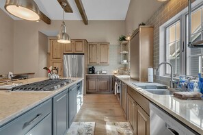 A modern kitchen with a central island, stainless steel appliances, wooden cabinets, and a large window providing natural light.
