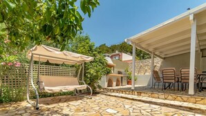 Un espace extérieur aménagé avec un sol en pierre, un coin salon abrité et un barbecue.