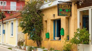 Un bâtiment sur lequel on peut lire l’inscription « Pergola Taverna 1980 », et de nombreux pots de plantes sont disposés le long du trottoir.