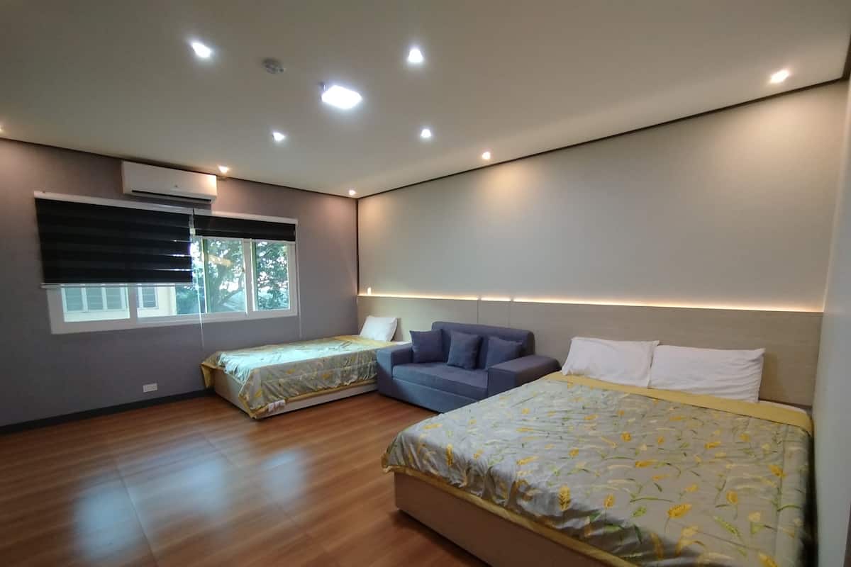 A modern bedroom with two single beds, a sofa, and a large window with blinds.