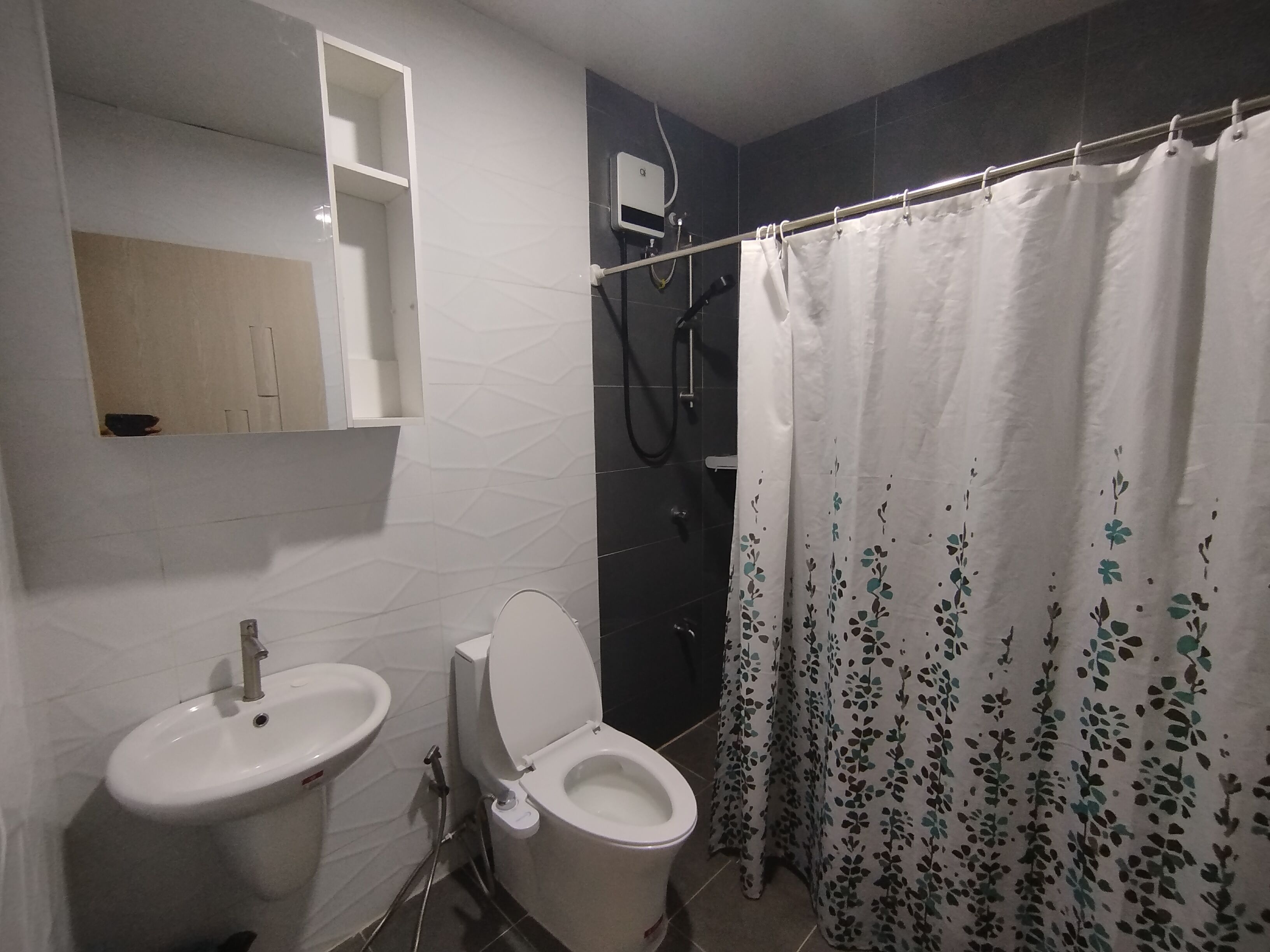 Et badeværelse med toilet, håndvask, bruser og spejl.