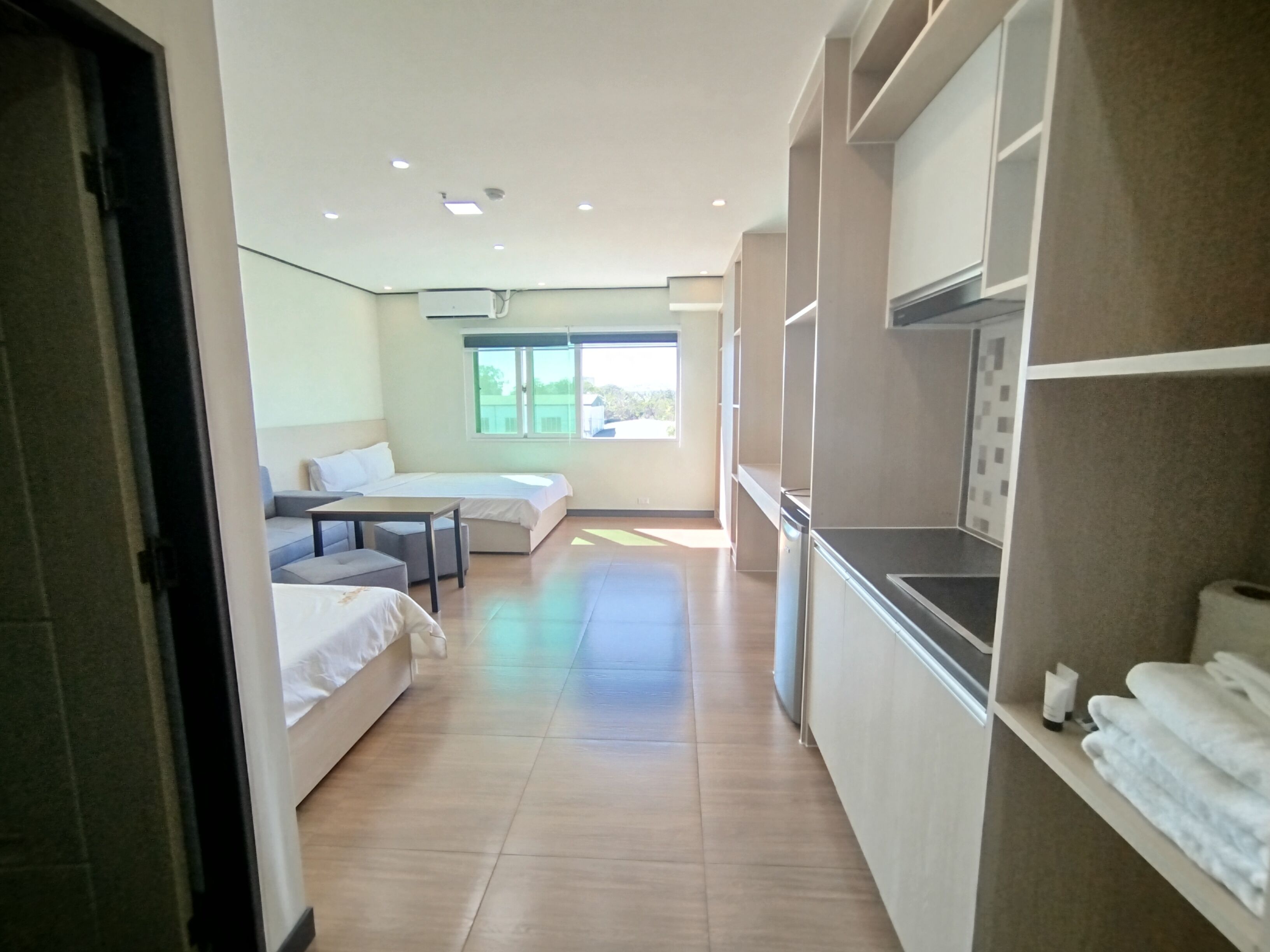 A modern hotel room with a bed, a sofa, a small table, and a kitchenette.