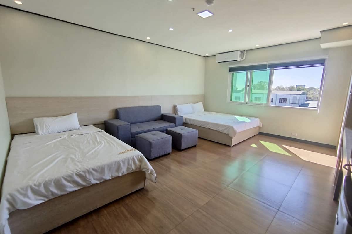 A modern hotel room with two beds, a sofa, and a window.