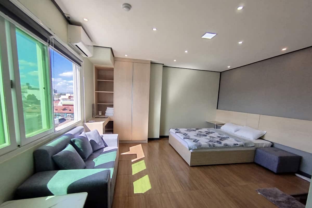 A modern hotel room with a bed, a sofa, a desk, and a large window.